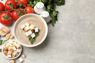 Delicious mushroom cream soup with croutons, parsley and ingredients on gray textured table, flat lay. Space for text