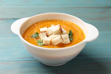 Tasty pumpkin cream soup with croutons and parsley in bowl on light blue wooden table, closeup