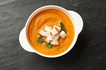 Tasty pumpkin cream soup with croutons and parsley in bowl on dark textured table, top view