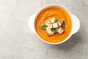 Tasty pumpkin cream soup with croutons and parsley in bowl on grey textured table, top view. Space for text