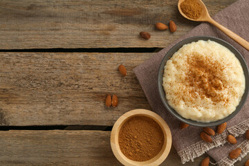 Delicious rice pudding with cinnamon and almonds on wooden table, flat lay. Space for text