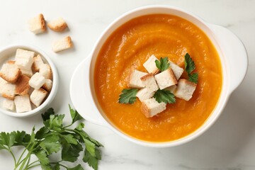 Tasty pumpkin cream soup with croutons and parsley in bowl on white table, flat lay