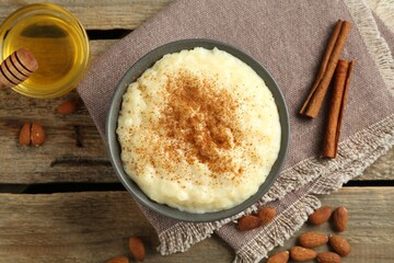 Delicious rice pudding with cinnamon, honey and almonds on wooden table, flat lay