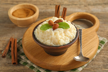 Delicious rice pudding with almonds, mint and cinnamon sticks served on wooden table, closeup