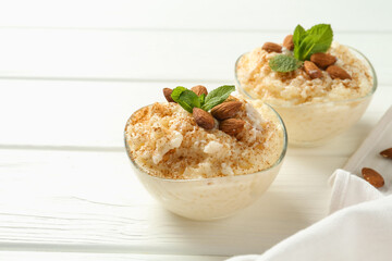 Delicious rice pudding with cinnamon, almonds and mint on white wooden table, closeup. Space for text