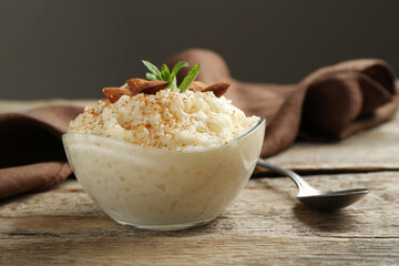 Delicious rice pudding with cinnamon, almonds and mint served on wooden table, closeup