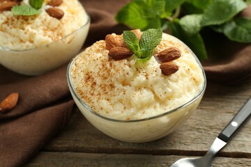 Delicious rice pudding with cinnamon, almonds and mint served on wooden table, closeup