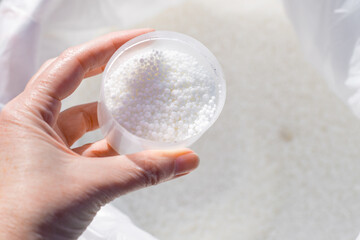 A woman's hand holding a measuring cup filled with mineral fertilizer granules, taken out of a bag....
