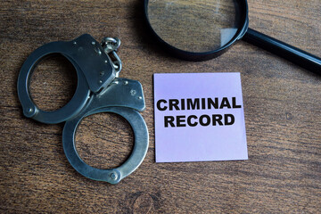 Concept of Criminal Record write on sticky notes and handcuff isolated on Wooden Table.