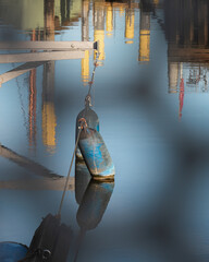 Blue fender floating on calm harbor water with colorful reflections
