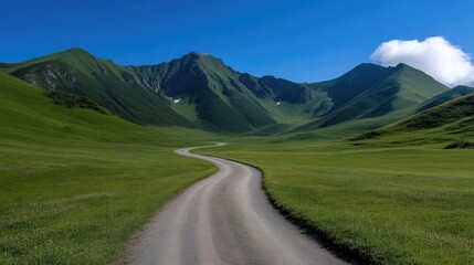 Winding road through lush green mountains.  A scenic dirt road meanders through a valley, surrounded by rolling hills covered in vibrant green grass.