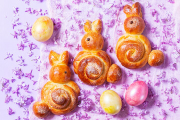 Easter composition made of sweet buns in the shape of a rabbit, eggs and lilacs.