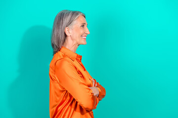 Confident mature woman in orange blouse smiling against a teal background, showcasing style,...