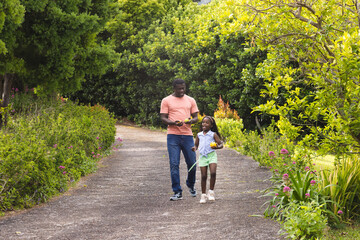 African American father and daughter walking dog on garden path, enjoying sunny day