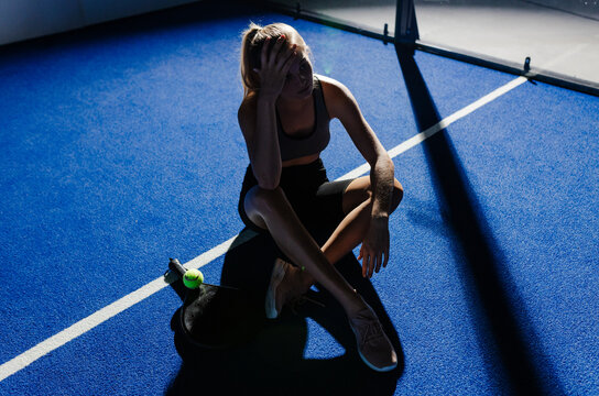 Exhausted female athlete sitting on padel court, holding head in frustration