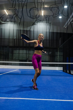 Woman playing padel tennis on indoor court, focused and ready to hit ball