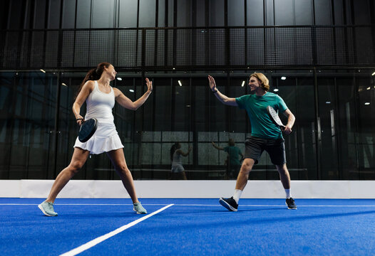 Mixed doubles team playing padel tennis, exchanging high fives on blue court