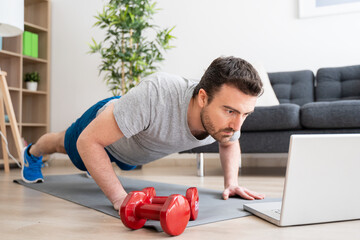 Man doing exercise while watching tutorial on laptop at home