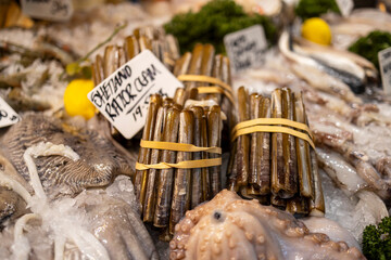 Fresh razor clams and other seafood displayed on ice at a market stall