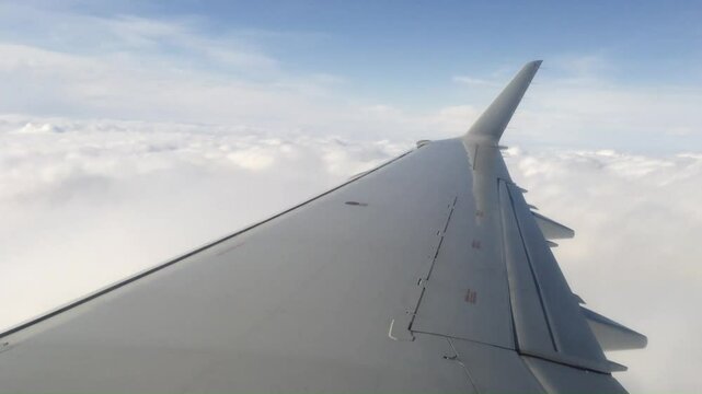 The wing of a passenger aircraft as it flies over a layer of fluffy while clouds.