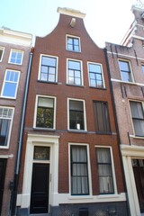 Historic brick building under clear blue sky in Amsterdam showcasing traditional Dutch architecture with tall windows and unique gable design, adding charm to the cityscape