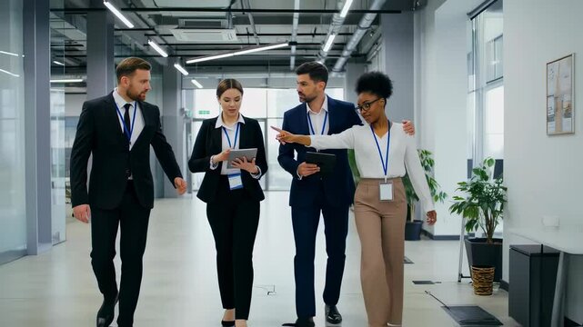 Business people standing in office lobby. A group of four people are walking down a hallway, one of them holding a tablet