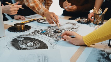 A group of engineers engaged in a creative workshop, actively analyzing detailed technical drawings...
