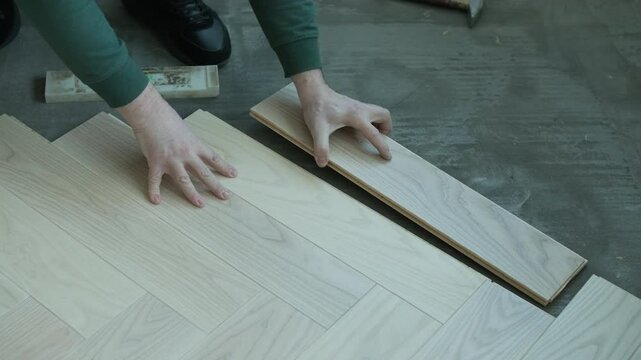 Worker installing wooden flooring with hammer and tapping block