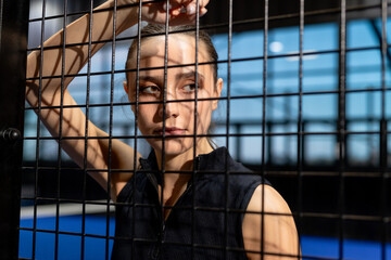 Focused woman standing behind padel court fence, contemplating game strategy