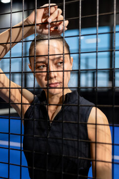 Focused woman standing by padel court fence, contemplating game strategy
