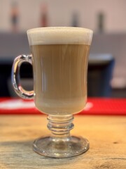 Savoring a Delicious Latte Crafted in a Clear Glass While Relaxing on a Wooden Table. A beautifully crafted latte served in a clear glass, presenting delicious layers of coffee and froth