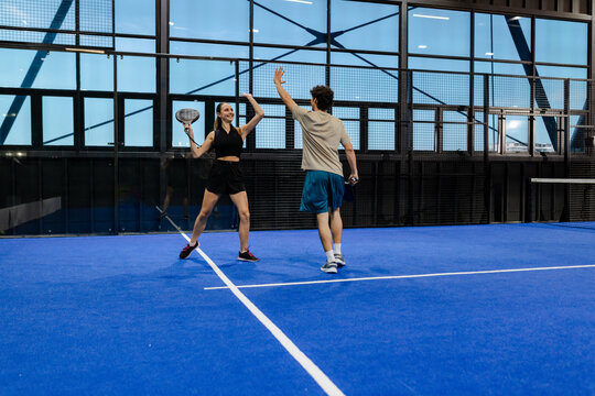 Celebrating victory, two players high-fiving on indoor padel tennis court - Powered by Adobe