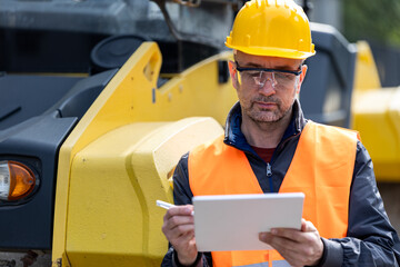 Construction worker wearing safety gear inspects equipment on site in bright daylight