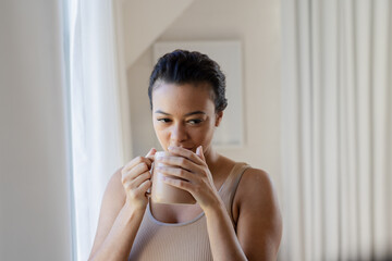 Woman enjoying coffee by window, relaxing and savoring peaceful morning moment