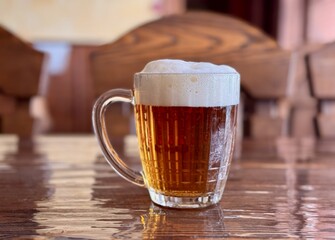 A Refreshing Glass of Beer is Poured on a Wooden Table, Perfectly Set for Enjoyment and Socializing. A frothy mug of icecold beer sits atop a beautifully polished wooden table, ideal for relaxation
