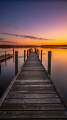 Naklejka premium A tranquil wooden pier stretching into a serene lake at sunset with soft pastel skies reflections.