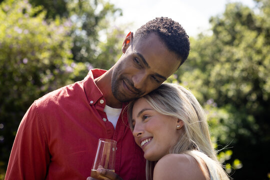 Diverse couple enjoying in garden party, smiling and holding glass in sunny garden, copy space