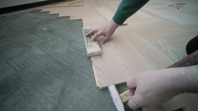 Worker installing wooden flooring with hammer and tapping block