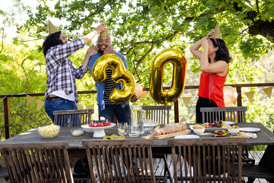 At party, Celebrating 30th birthday, diverse friends on deck with balloons, party hats, smiling joyf