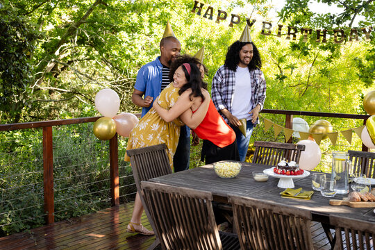 At party, Celebrating birthday on deck, diverse friends hugging and laughing near decorated table