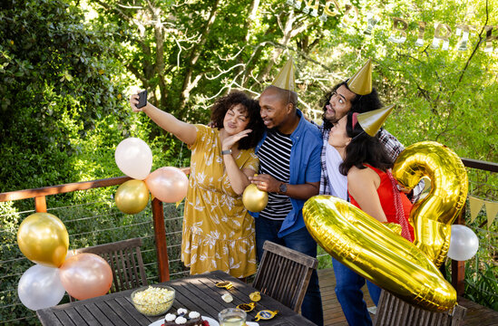 At party, Taking selfie with balloons and party hats, diverse friends celebrating on deck happily
