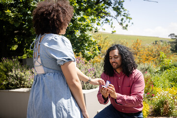 Man proposing with ring, woman surprised and happy in garden setting