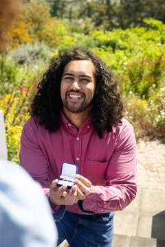 Man kneeling holding ring box, smiling and proposing in garden