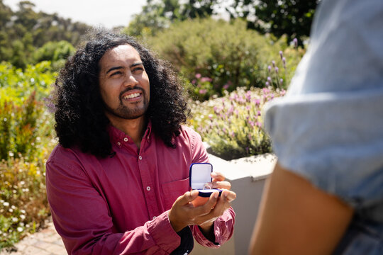 Man proposing with ring box in garden, smiling and looking hopeful