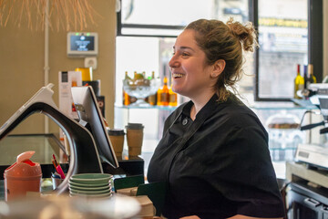 Smiling female barista attending customers at a coffee shop counter. Labor day concept