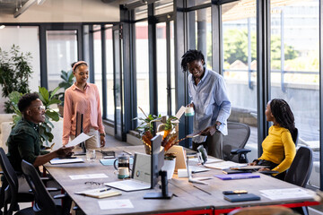 In modern office, diverse team discussing ideas and sharing documents collaboratively