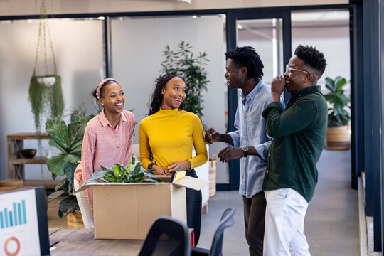 Diverse colleagues laughing and unpacking box with plants in modern office
