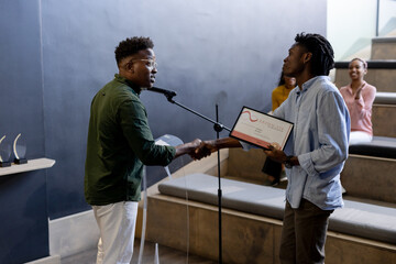 At office, Receiving certificate on stage, African American man applauded by audience at ceremony