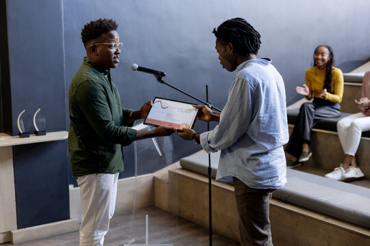 At office, On stage, two men presenting award while audience applauding enthusiastically