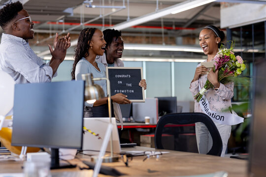 Diverse colleagues celebrating promotion with flowers and sign in modern office setting